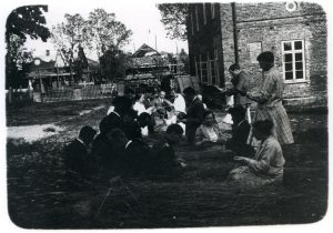 Telšiuose vykusių pedagoginių darbų kursų 1-os grupės dalyviai pynimo iš šiaudų pamokoje. Lektorė p. Dementijevienė. Motiejus Lukšys klūpi kairėje pusėje už moters šviesiais rūbais. Telšiai.1929 m. Nuotrauka iš Nijolės Lukšytės asmeninio archyvo