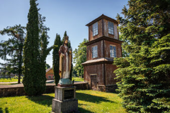 Kupreliškio Šv. arkangelo Mykolo bažnyčios medinė trijų tarpsnių varpinė ir Kristaus Karaliaus skulptūra šventoriuje. Fotogr. G. Lukoševičius. Kupreliškis (Biržų r.). 2025 m. PAVB skaitmeninis archyvas