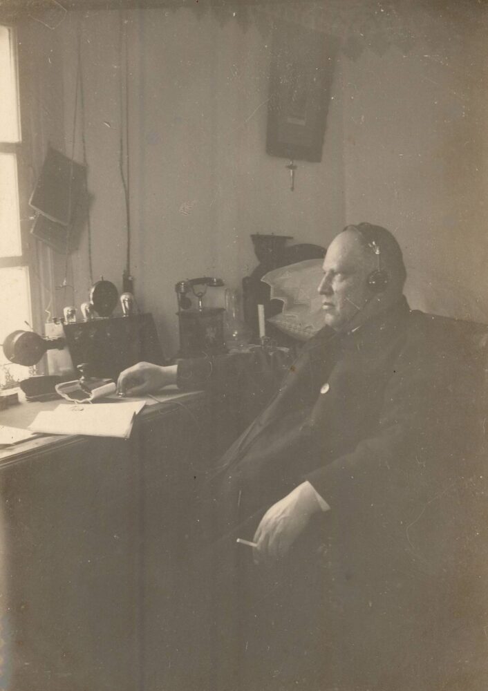 Raguvos Švč. Mergelės Marijos Ėmimo į dangų parapijos klebonas Jonas Maciejauskas savo darbo kambaryje klausosi radijo. Raguva (Panevėžio r.). Apie 1930 m. PAVB, Pavienių rankraščių fondas F8-660-3